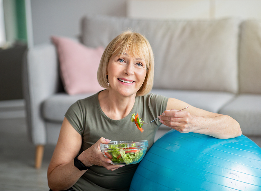 A senior woman smiles while eating. Implant-supported dentures provide stability that makes eating more comfortable.